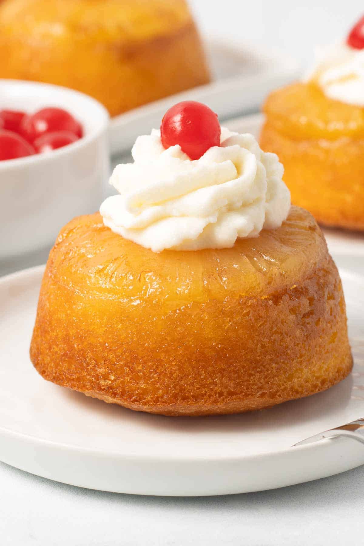 A small pineapple upside down cake topped with whipped cream and a cherry.
