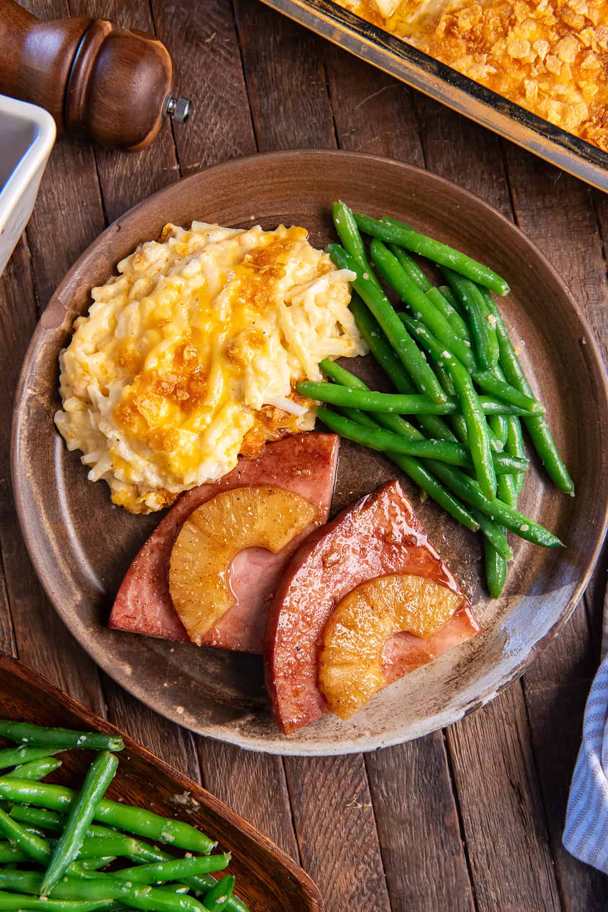 Pineapple glazed ham steak on a brown plate with cheesy hash browns and green beans.