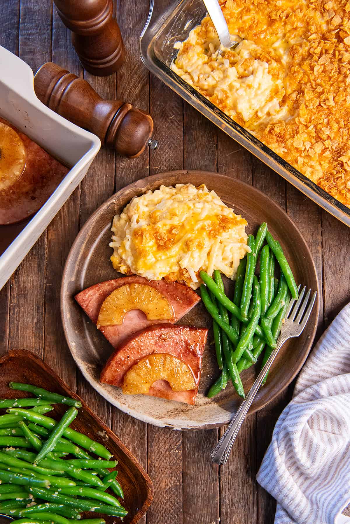 Pineapple ham steak on a brown plate with cheesy hash browns and green beans.