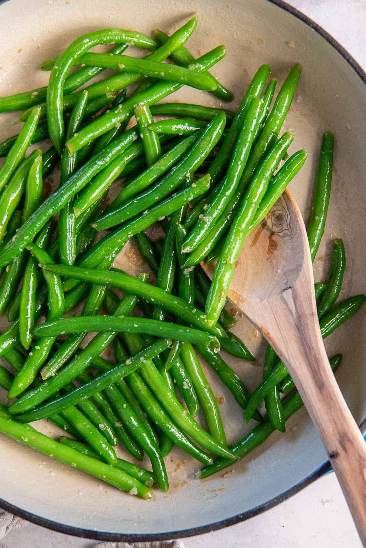 A wooden spoon resting in a pan of sauteed green beans.