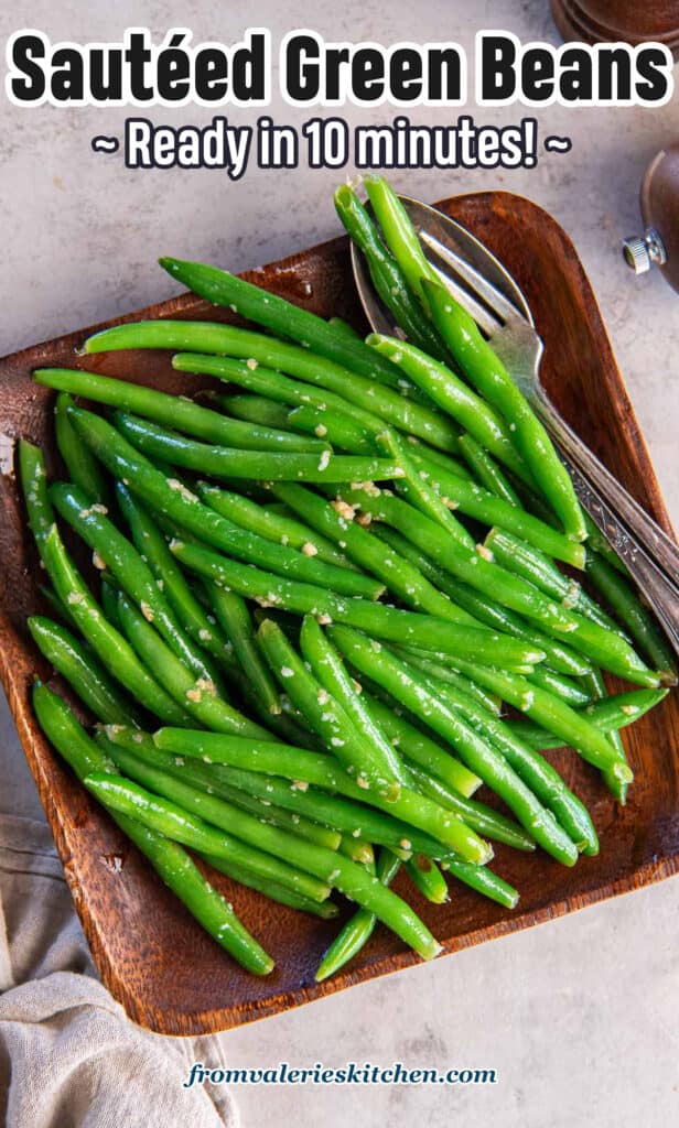 Sauteed green beans on a wood platter with text.