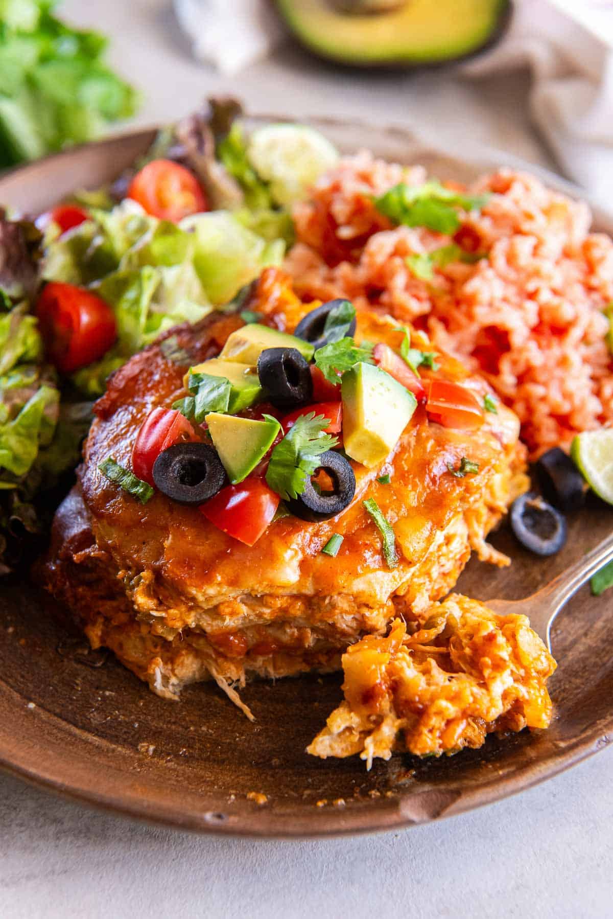 A fork resting on a plate with a serving of slow cooker chicken enchiladas, rice, and salad.