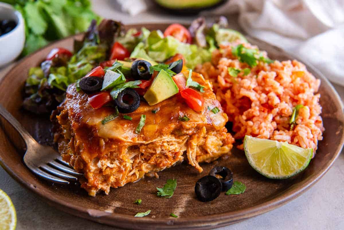 A wooden plate with a serving of slow cooker chicken enchiladas, rice, and salad.