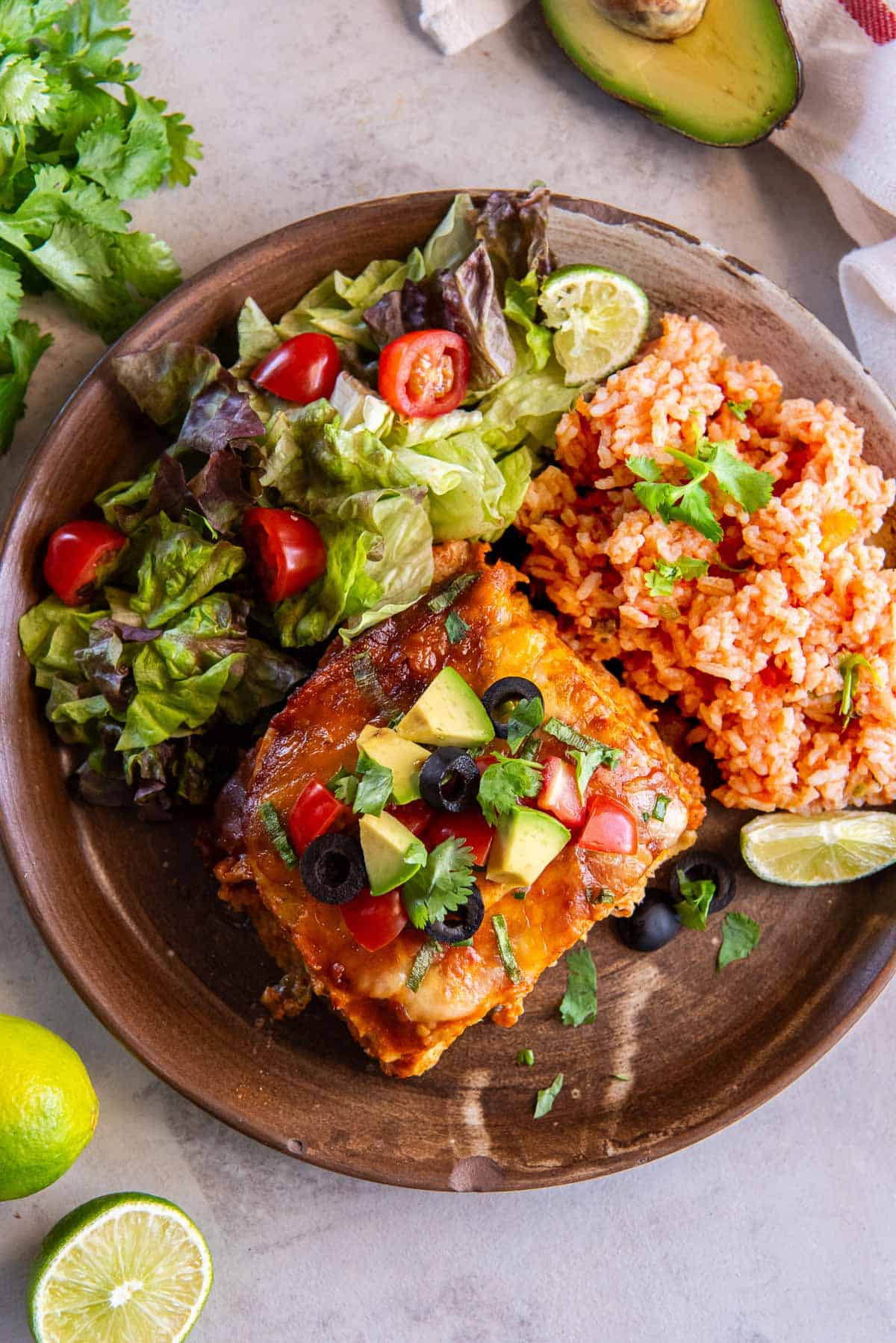 A wooden plate with a serving of slow cooker chicken enchiladas, rice, and salad.