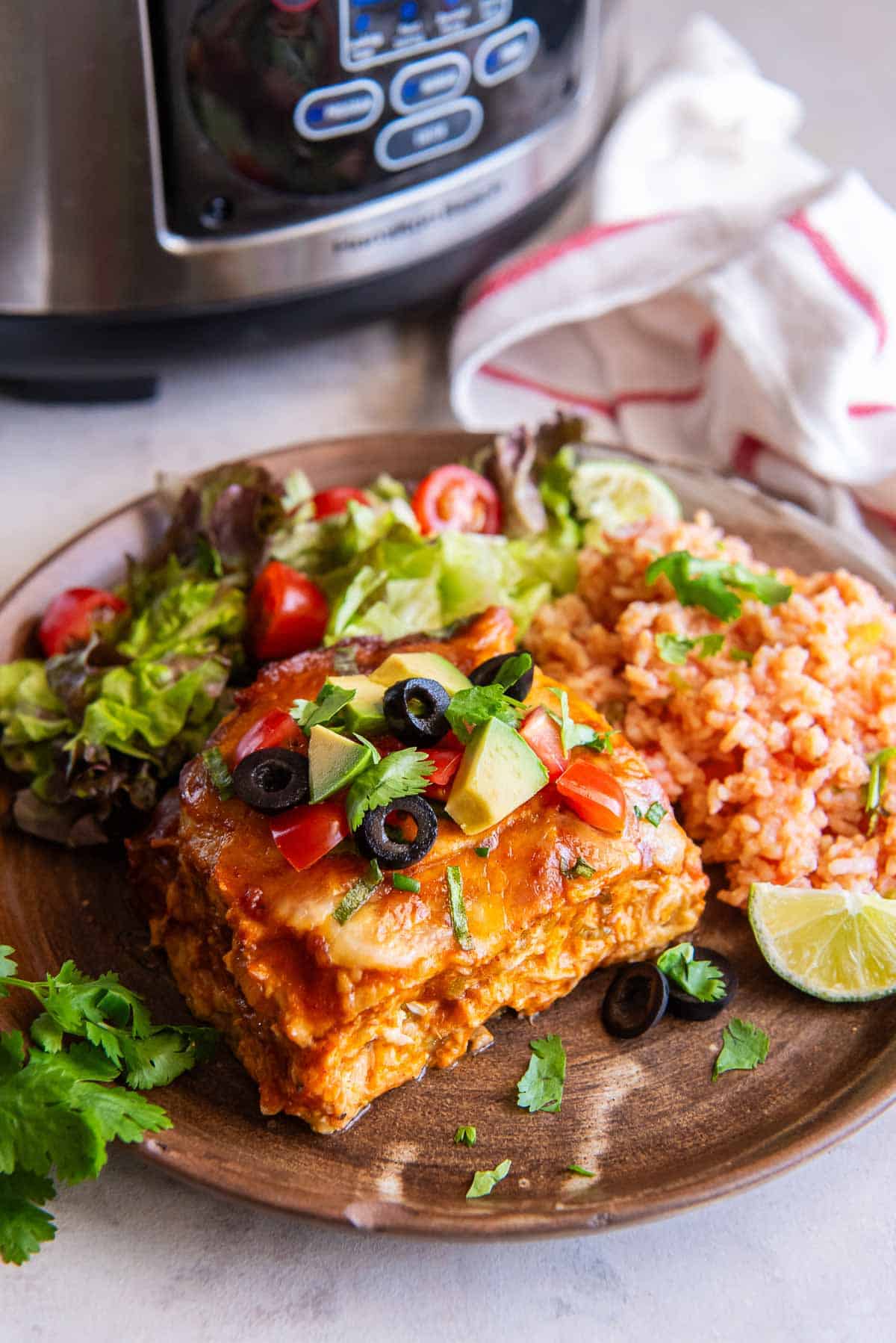 A wooden plate with a serving of slow cooker chicken enchiladas, rice, and salad.