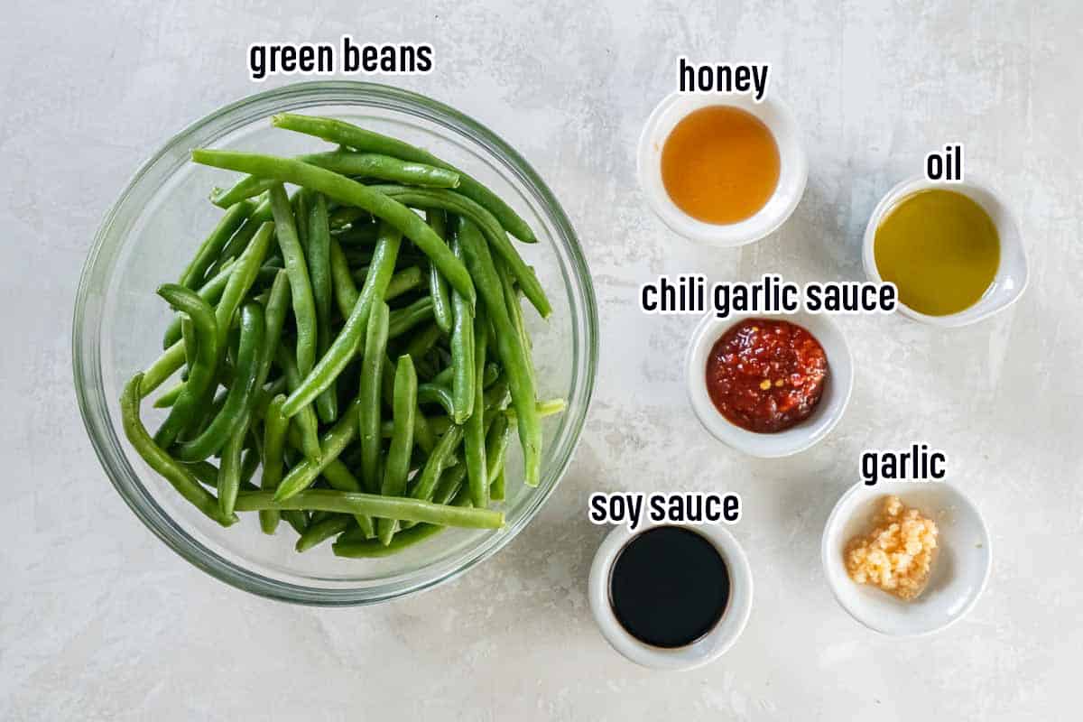 Green beans, honey, oil, soy sauce, garlic, and chili garlic sauce in bowls with text.