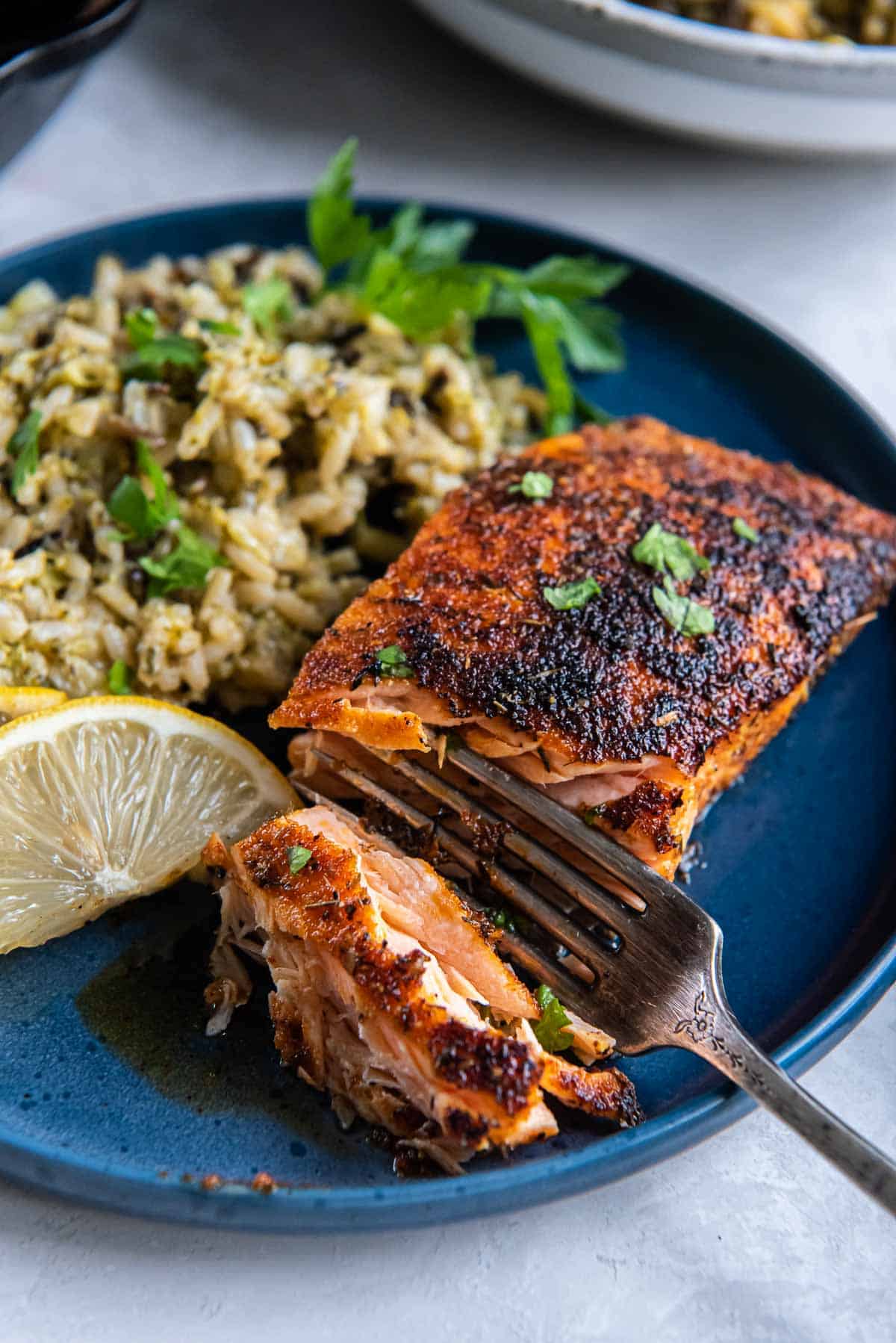 A fork breaking into a piece of blackened salmon a blue plate.