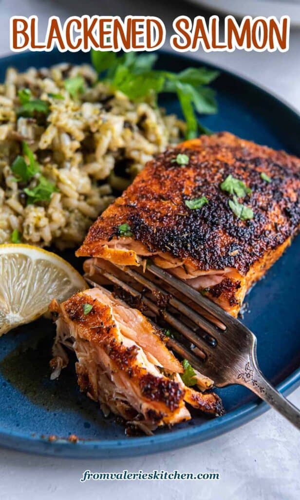 A fork breaking into a piece of blackened salmon a blue plate with text.