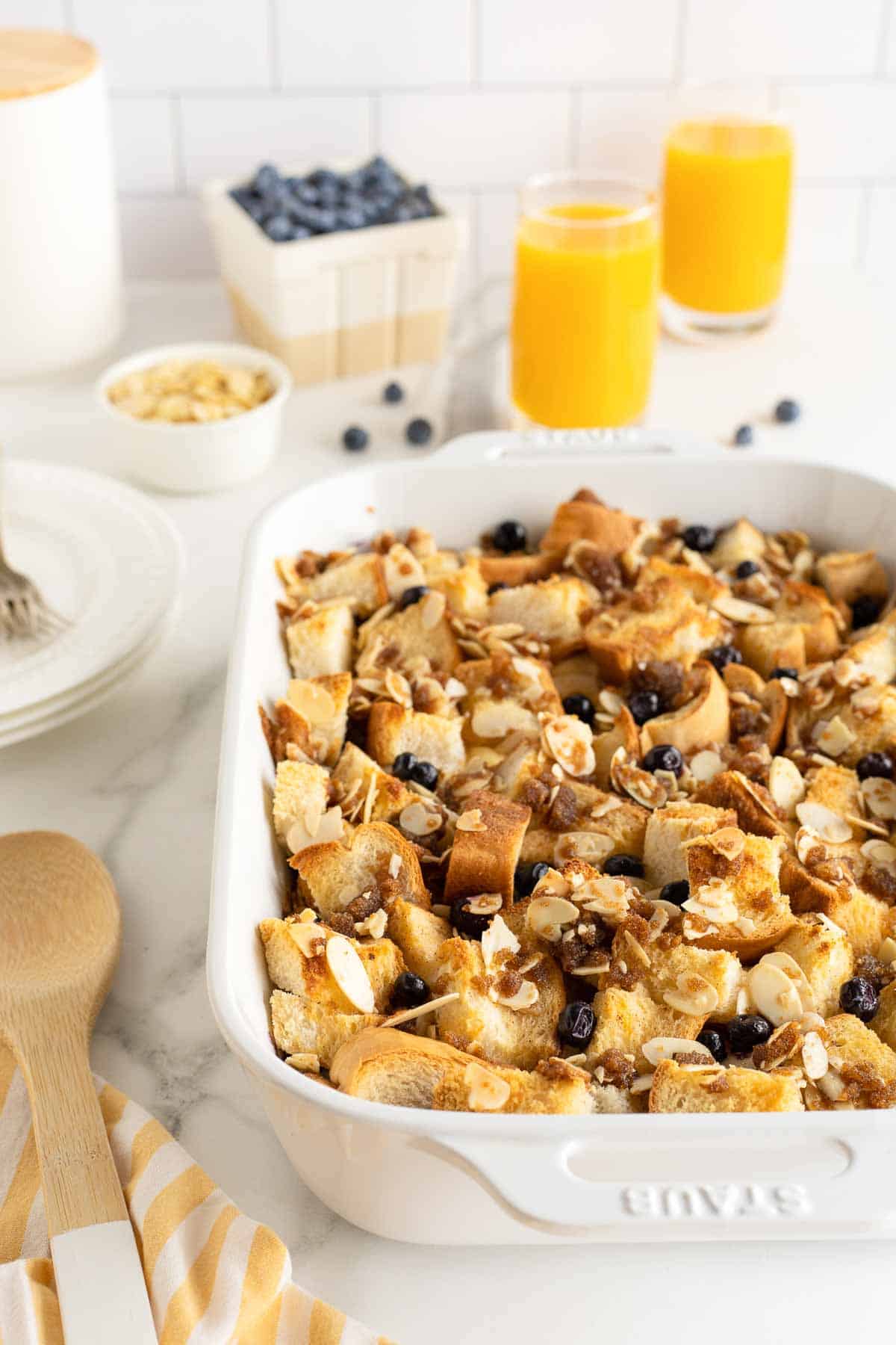 Blueberry French toast casserole in a white baking dish on a kitchen counter with glasses of orange juice.
