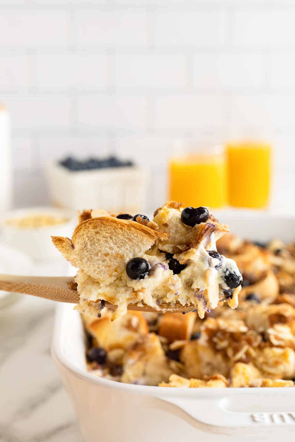 A wooden spoon scooping blueberry French toast casserole from a baking dish.