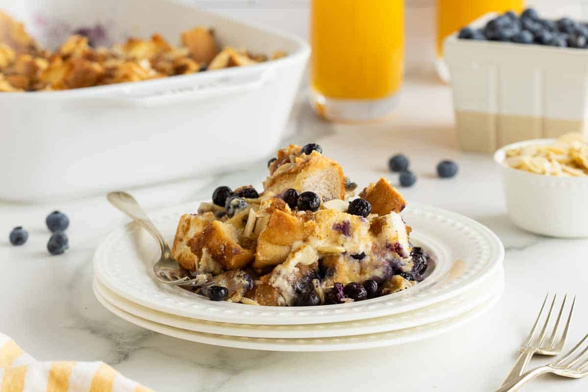 A serving of blueberry French toast casserole on a stack of white plates on a kitchen counter.