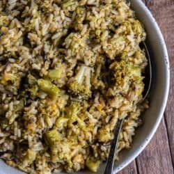 A serving spoon resting in a bowl of broccoli cheese rice.