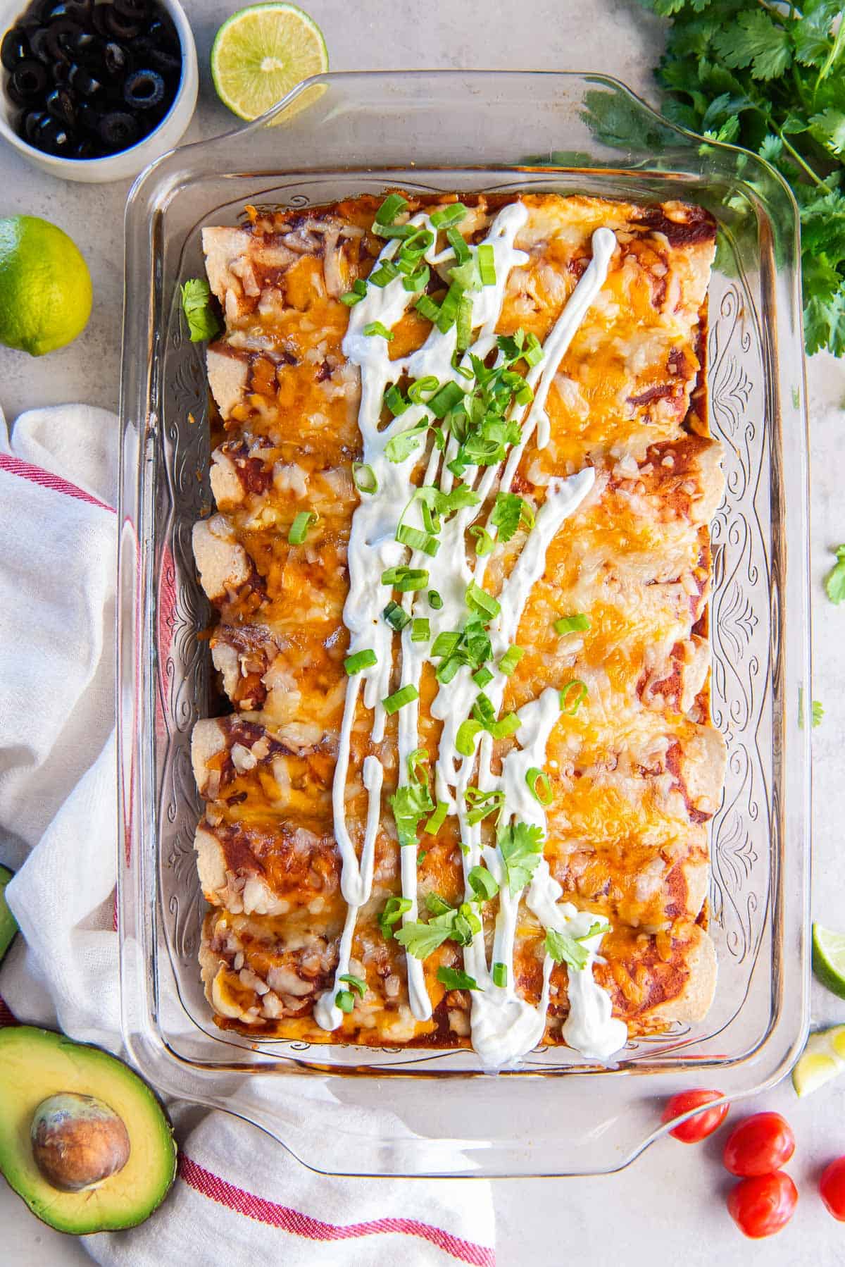 Chicken enchiladas in a baking dish topped with sour cream and sliced green onions.