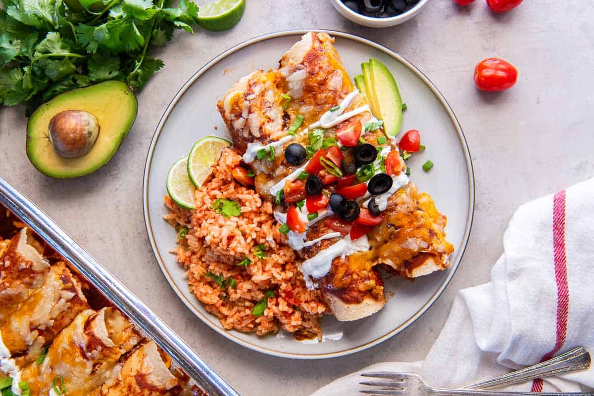 Two chicken enchiladas on a dinner plate with mexican rice.