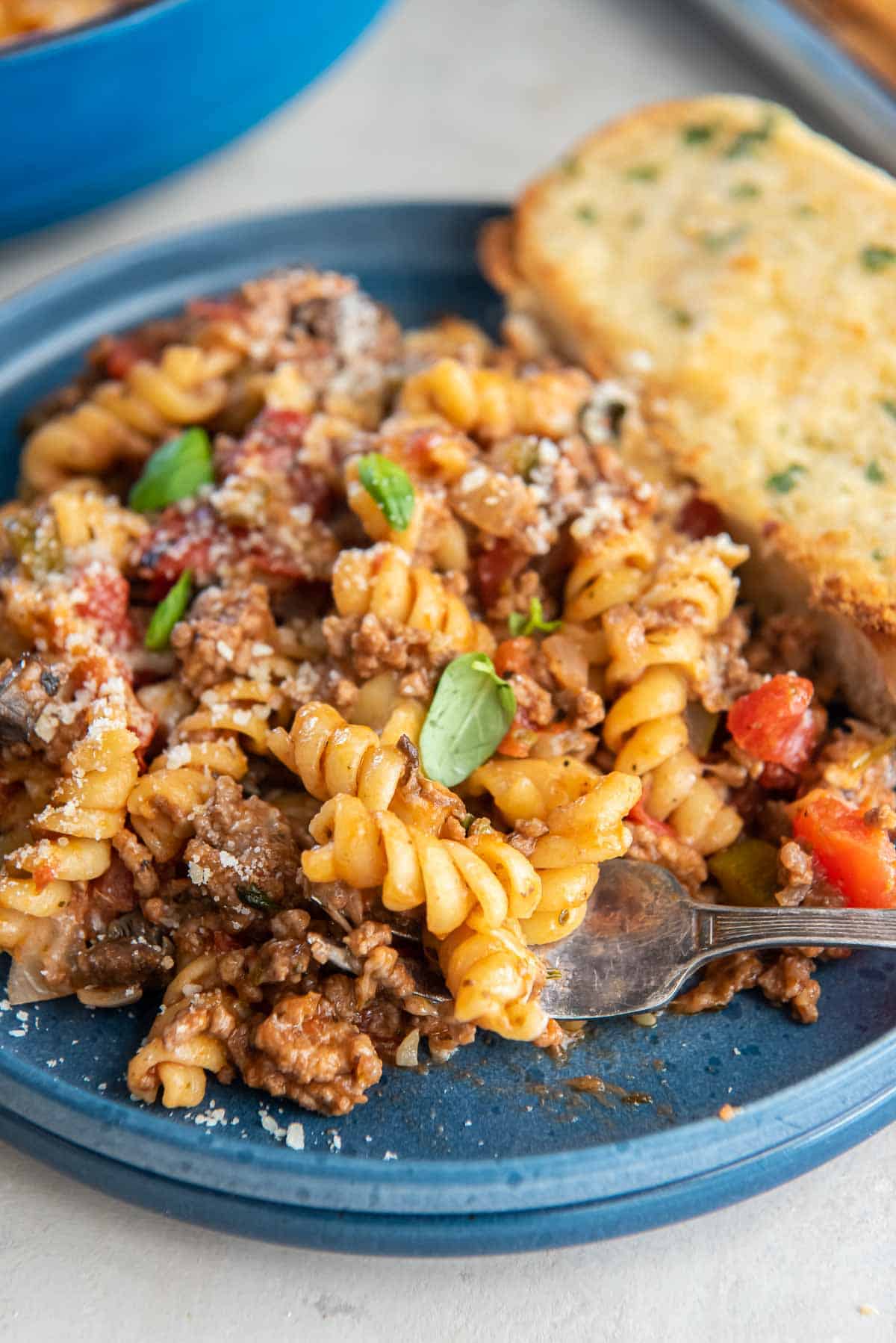 A fork scooping some ground beef pasta from a blue plate.