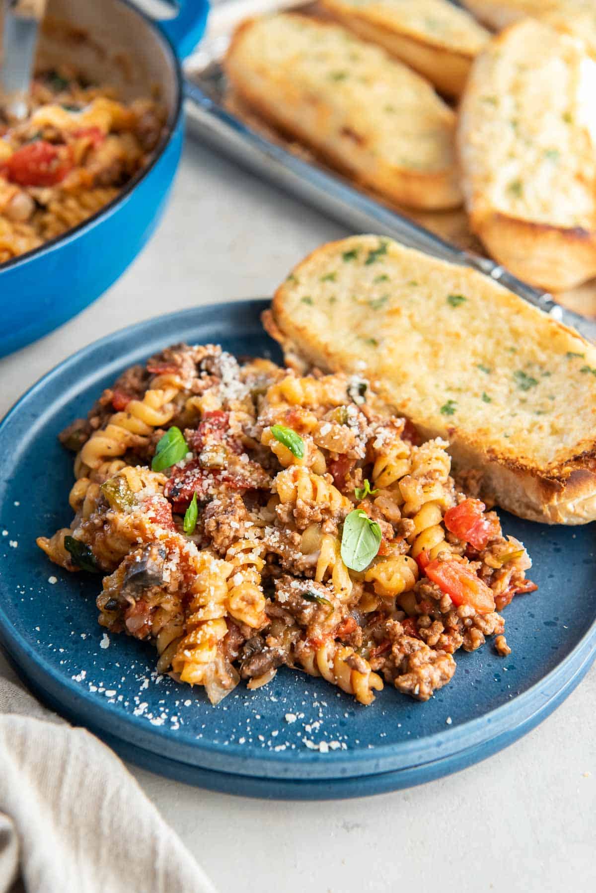 A serving of ground beef pasta on a blue plate with garlic bread.