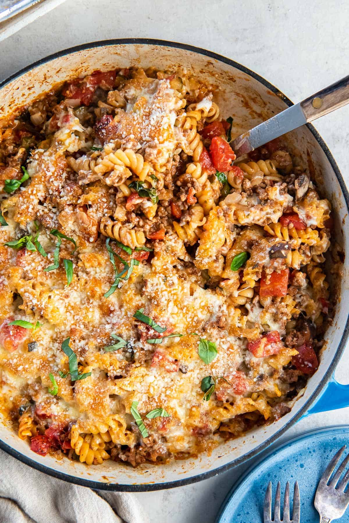 A spoon resting in a skillet of ground beef pasta.