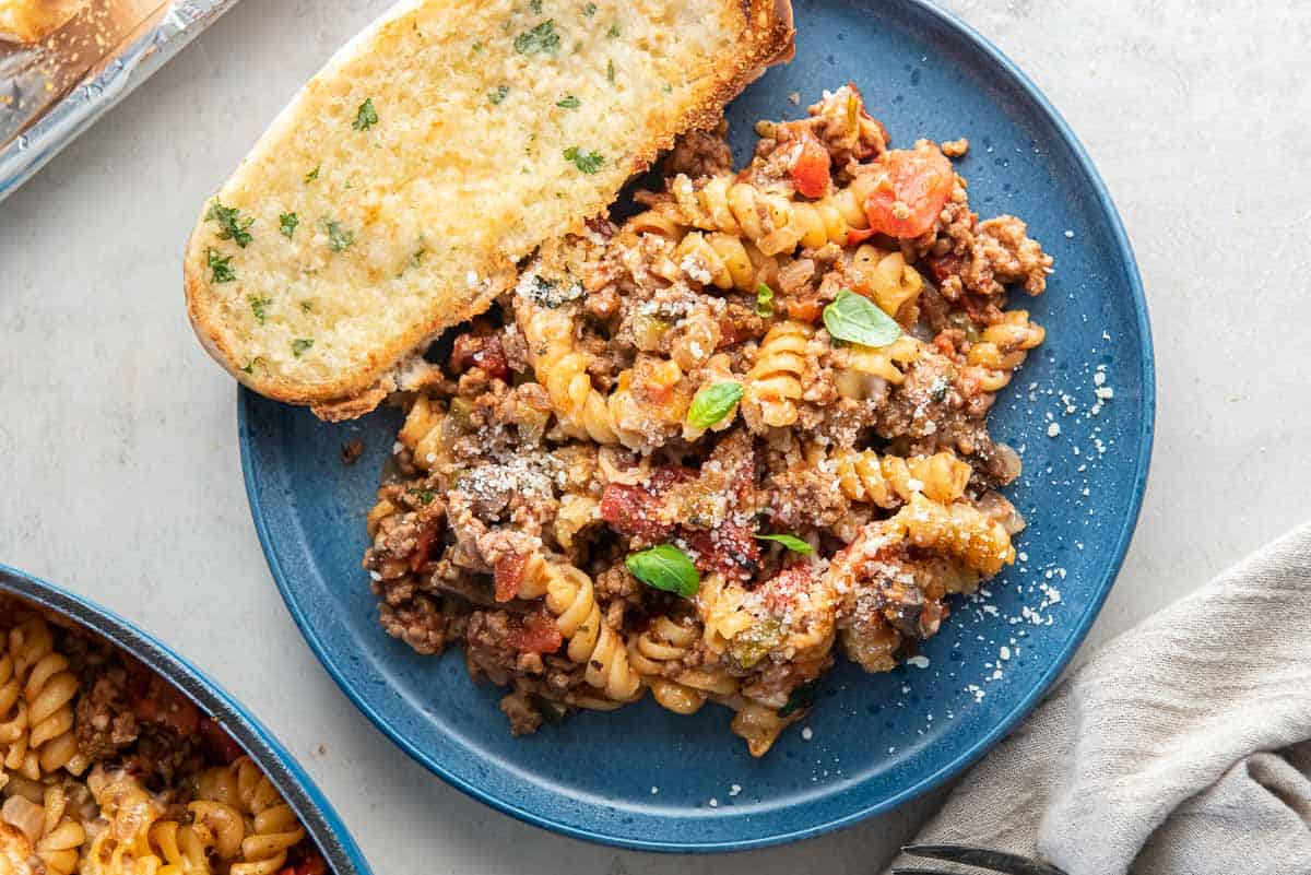 A serving of ground beef pasta on a blue plate with garlic bread.