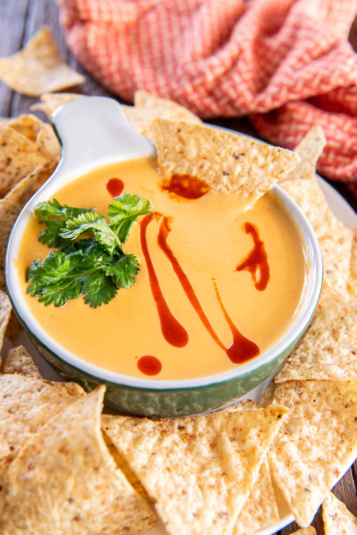 A tortilla chip dipping into a small dish of nacho cheese sauce.