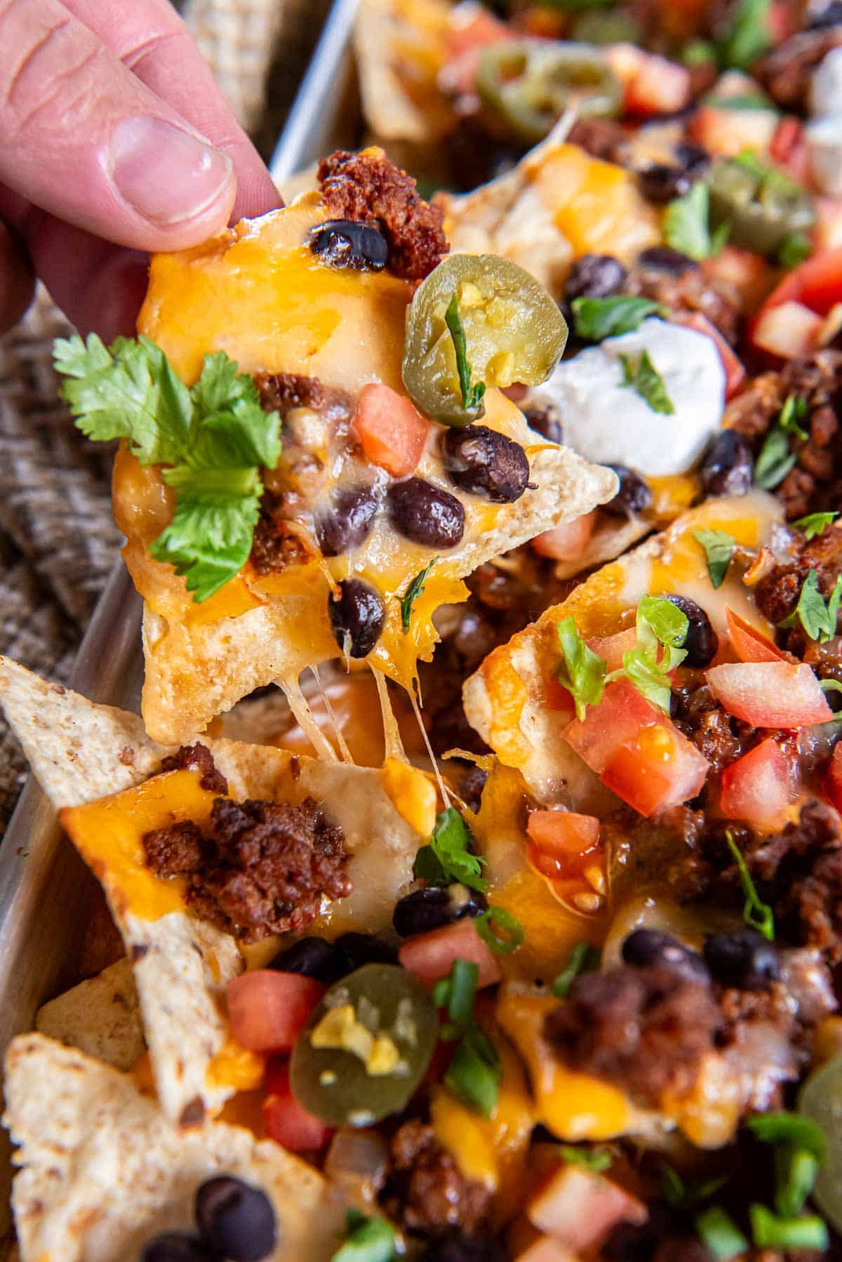 Fingers pulling a cheesy tortilla chip from nachos on a sheet pan.