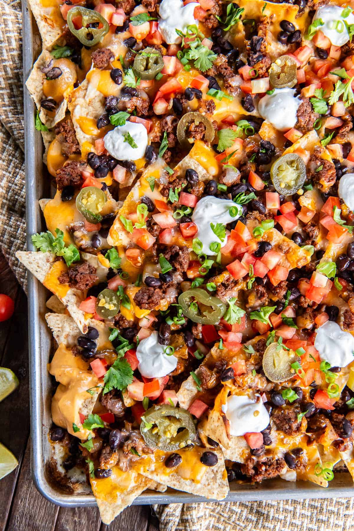 Nachos with ground beef, nacho cheese sauce, tomatoes and sour cream on a baking sheet.
