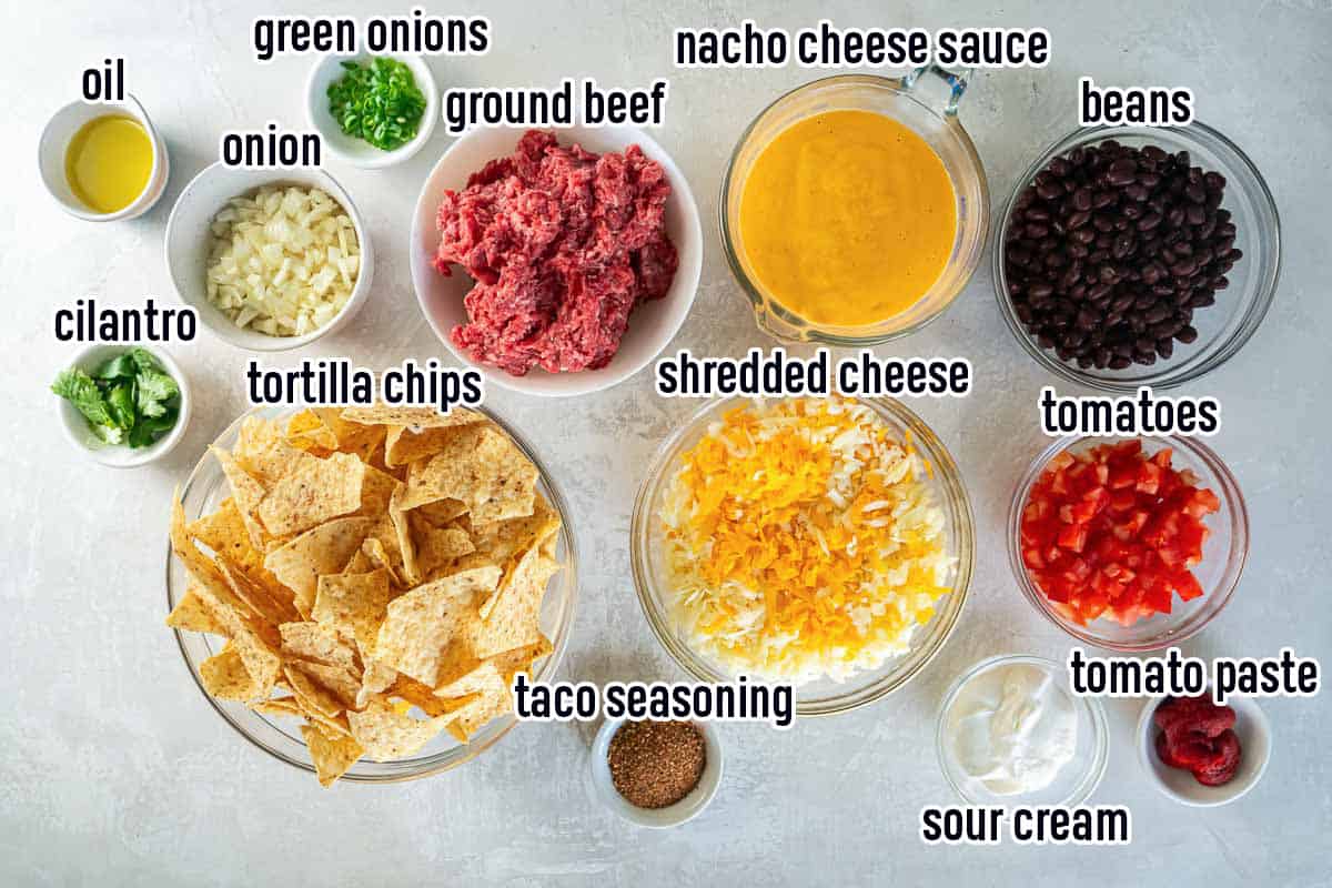 Ground beef, tortilla chips, cheese and other ingredients for nachos with text.