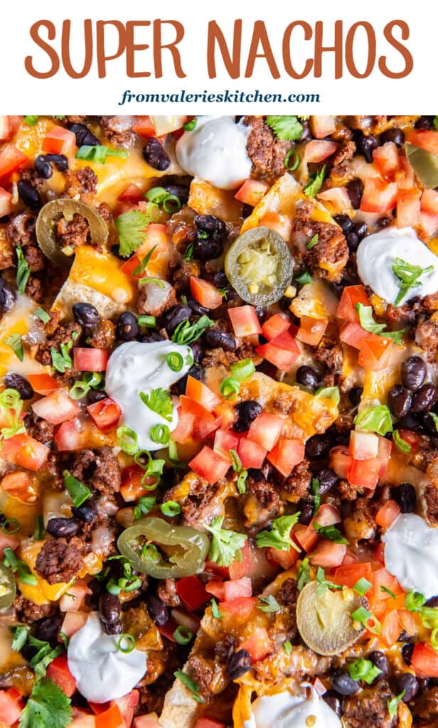 Nachos with ground beef, nacho cheese sauce, tomatoes and sour cream on a baking sheet with text.