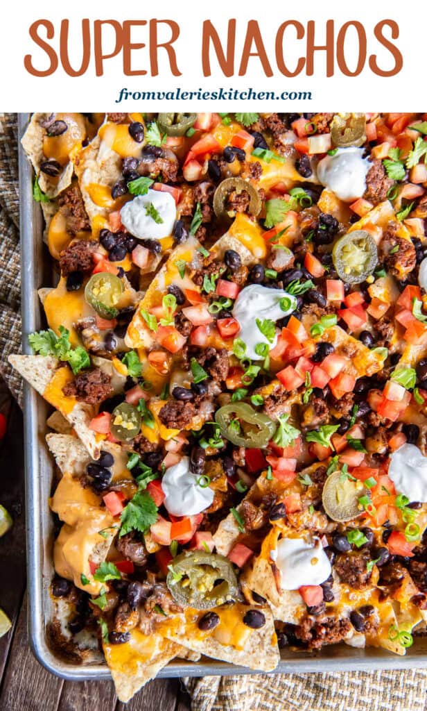 Nachos with ground beef, nacho cheese sauce, tomatoes and sour cream on a baking sheet with text.