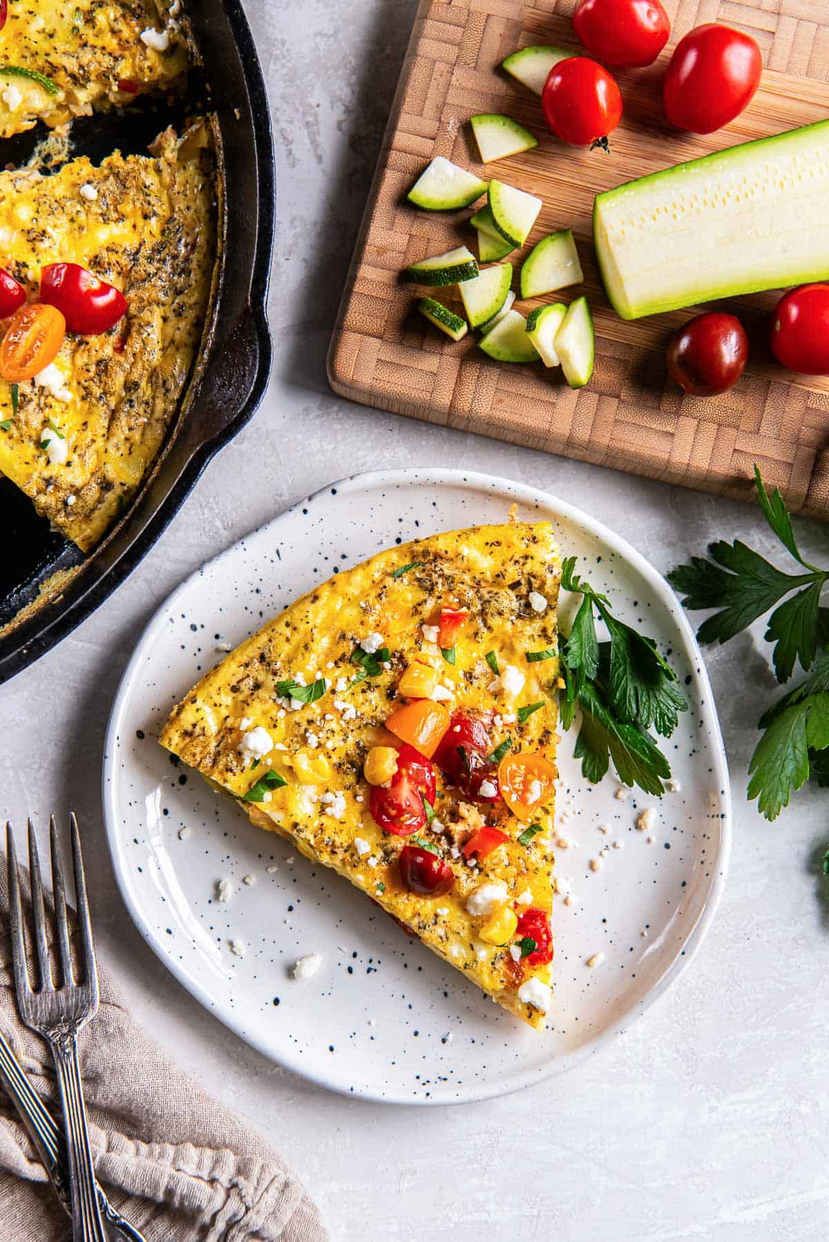 A slice of zucchini frittata on a white plate next to a cast iron skillet.