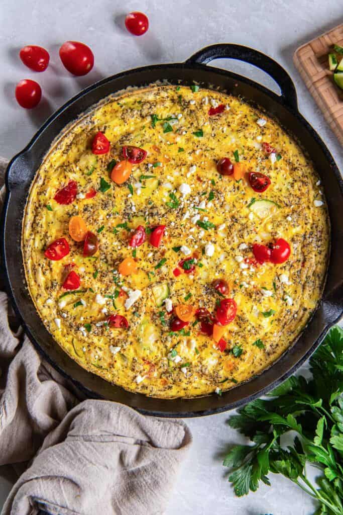 Zucchini frittata with cherry tomatoes, corn, and feta in a cast iron skillet.