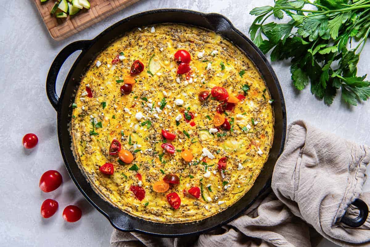 Zucchini frittata with cherry tomatoes, corn, and feta in a cast iron skillet.