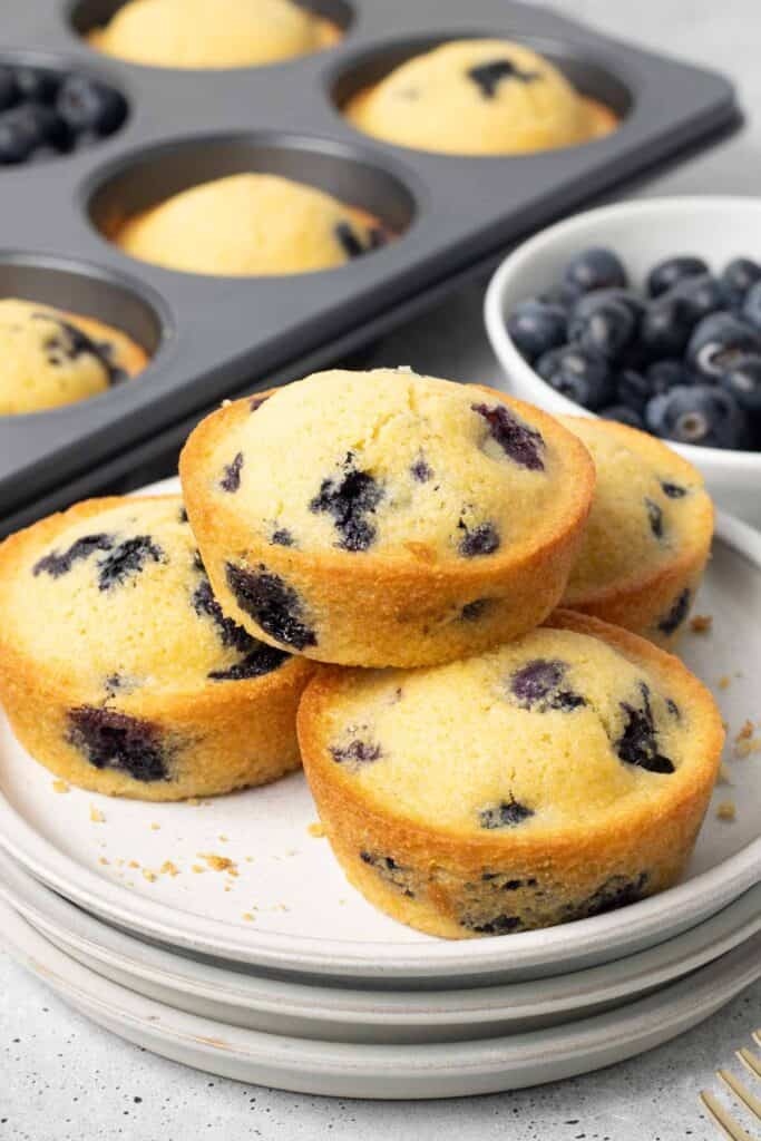 Three blueberry cornmeal muffins on a stack of white plates.