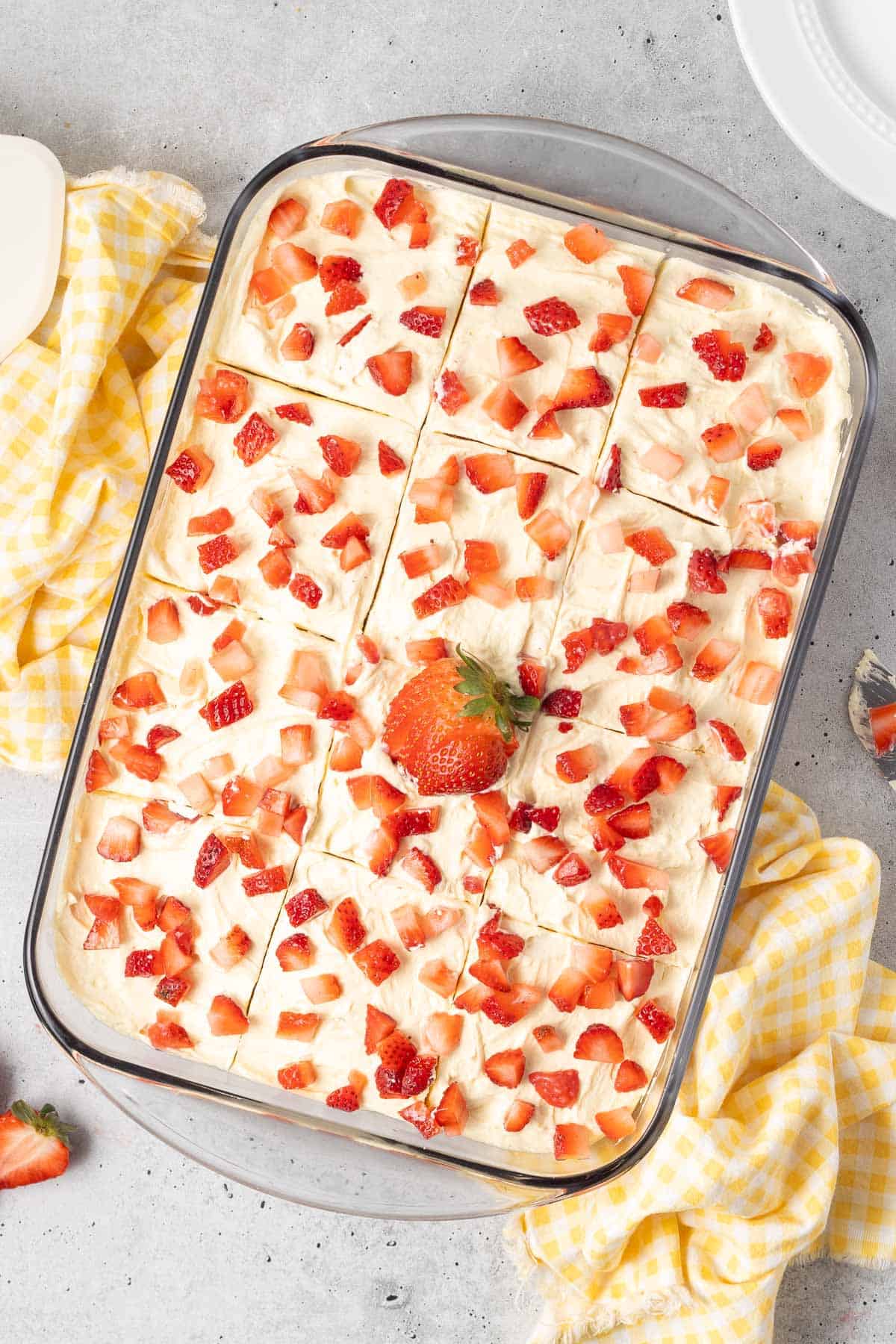 Jello cake in a baking dish topped with frosting and fresh strawberries.