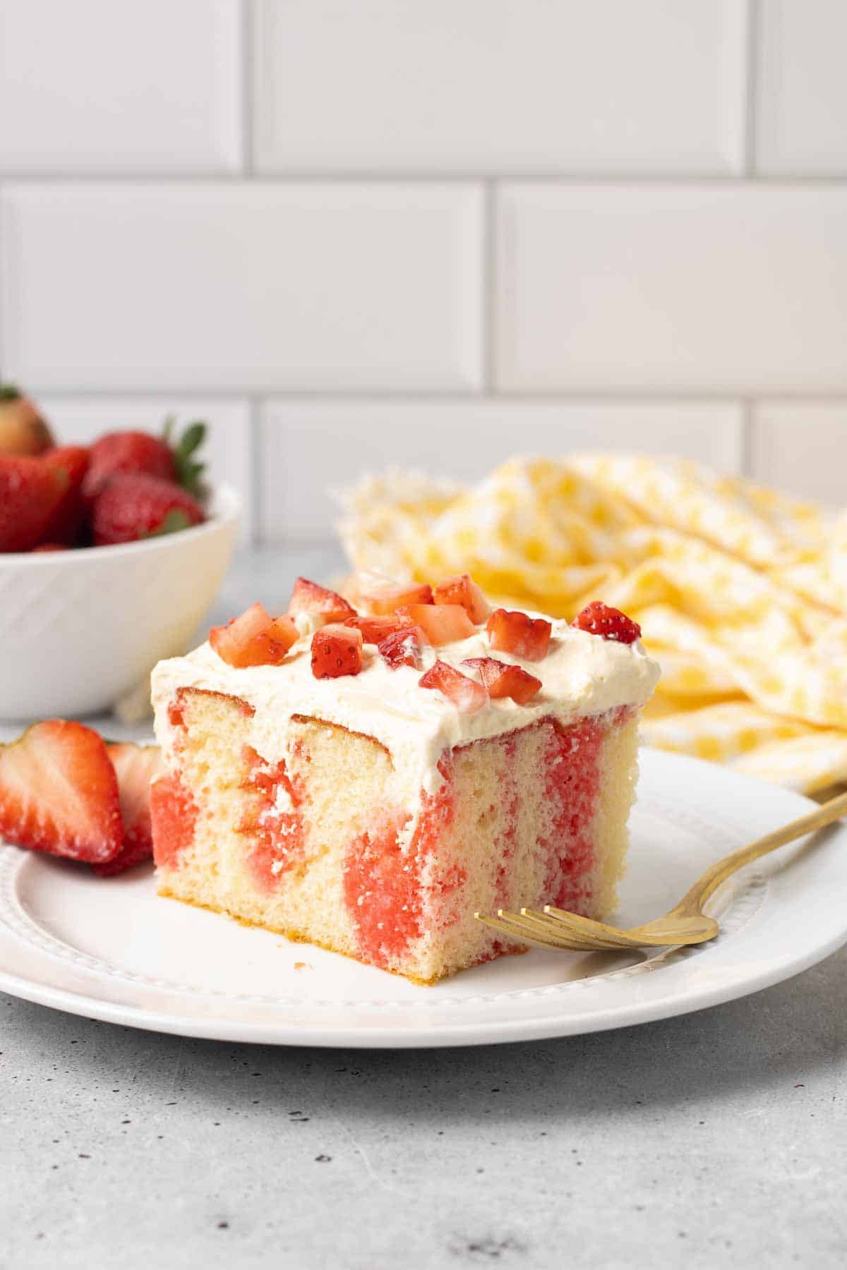 A fork resting on a plate with a slice of jello cake topped with strawberries.