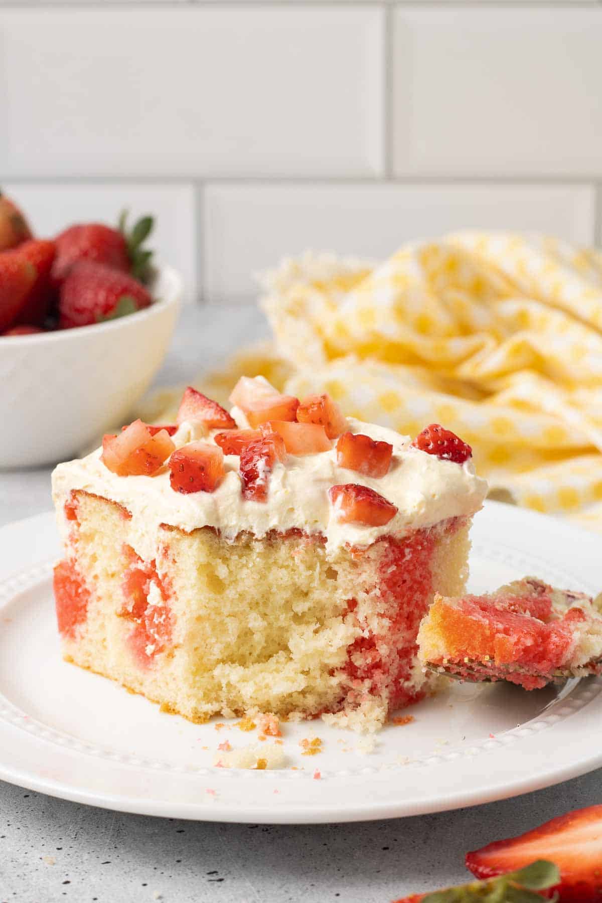 A fork holding a bite of cake resting on a plate with a slice of jello cake.