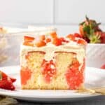 A fork resting on a plate with a slice of jello cake topped with strawberries.