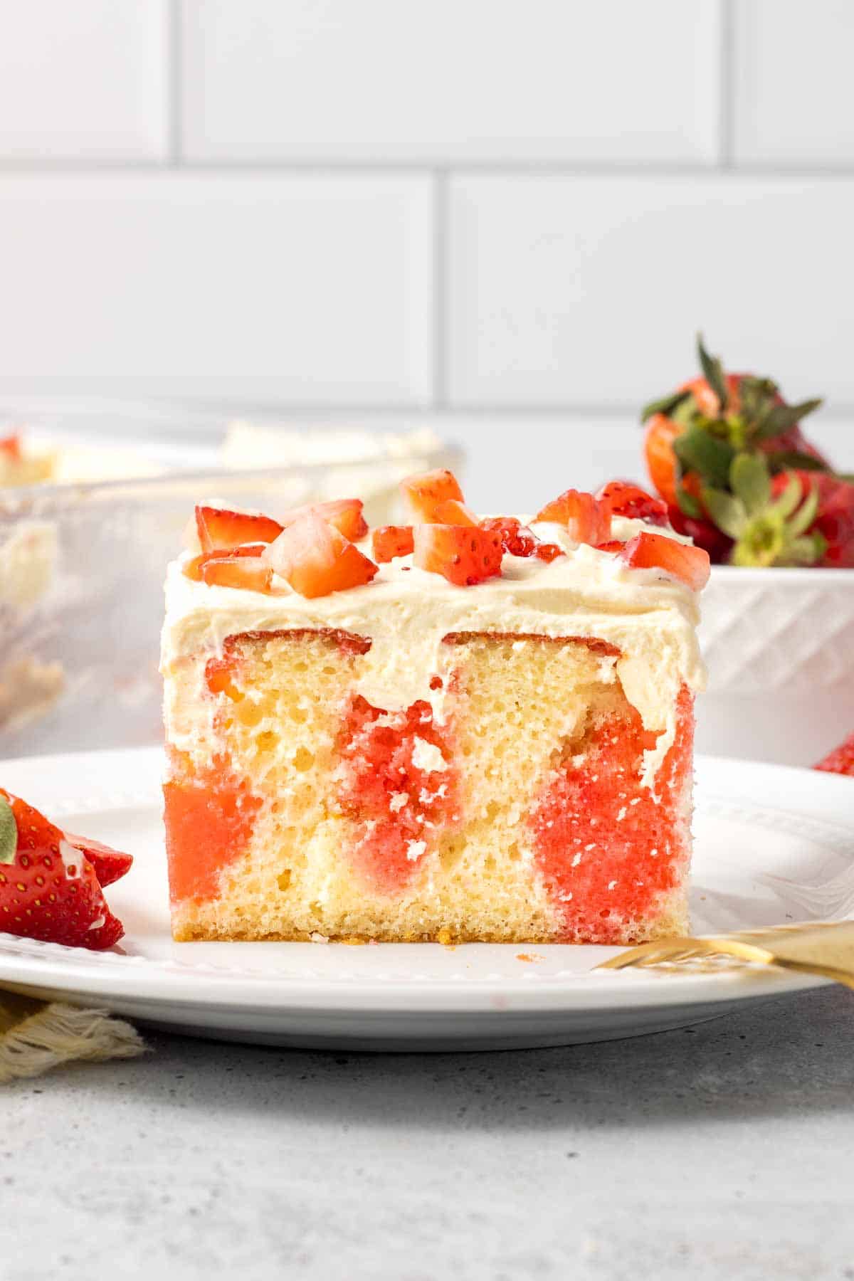 A fork resting on a plate with a slice of jello cake topped with strawberries.
