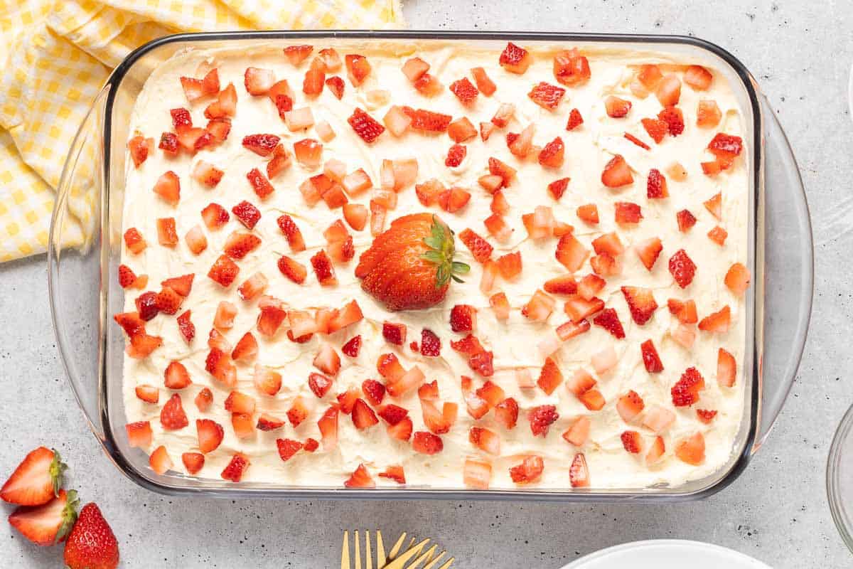 Jello cake in a baking dish topped with frosting and fresh strawberries.