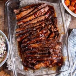 Sliced brisket with bbq sauce in a baking pan surrounded by other dishes.