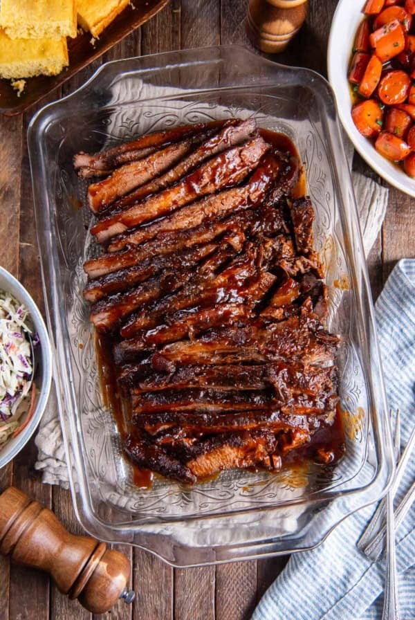 Sliced brisket with bbq sauce in a baking pan surrounded by other dishes.