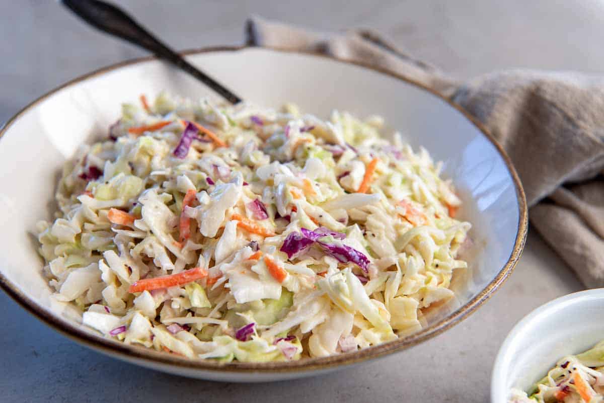 A bowl of coleslaw on a kitchen counter next to a kitchen cloth.