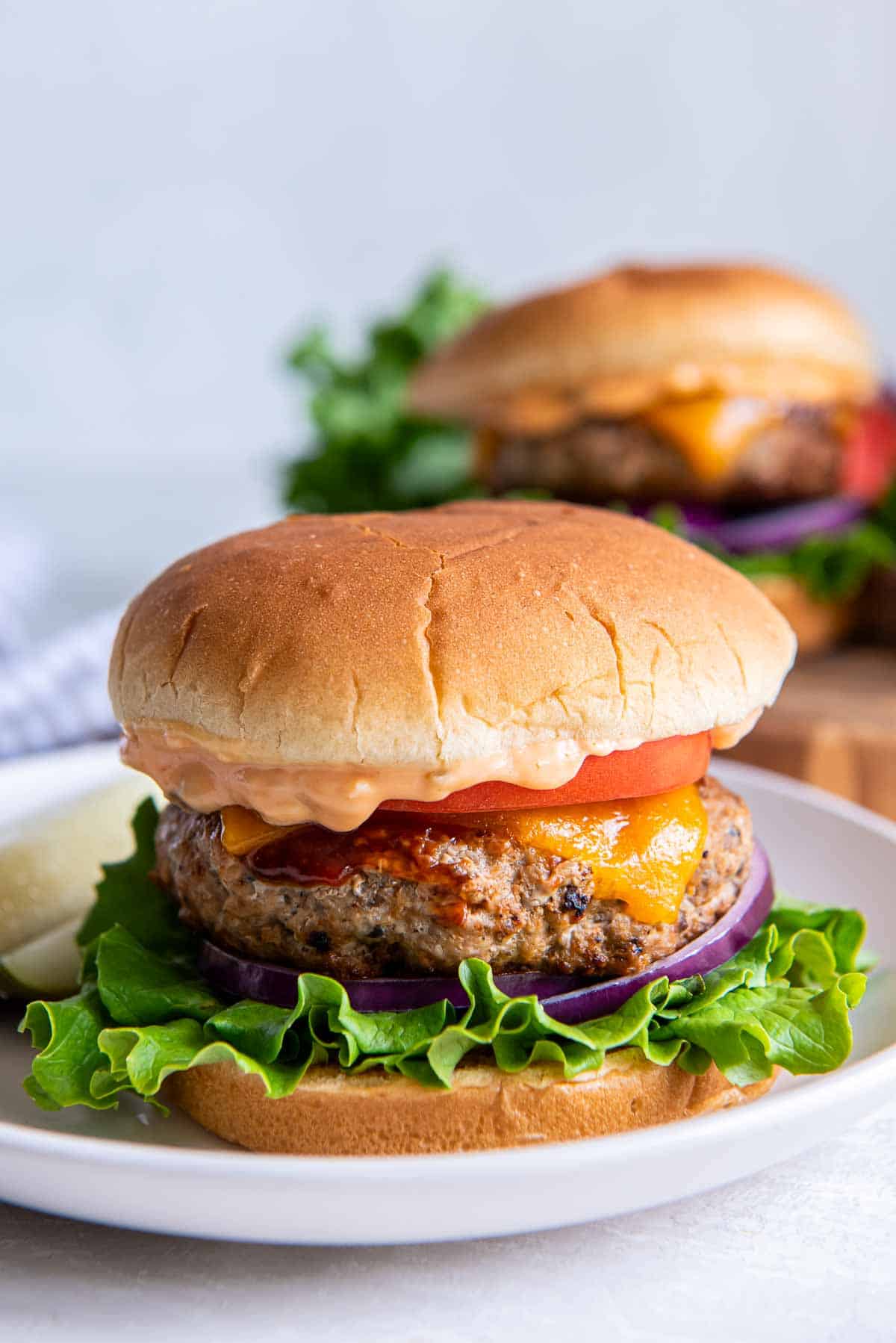 A turkey burger with cheese, lettuce, and tomato on a bun on a white plate.