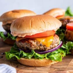 Turkey burgers with cheese, tomato, and lettuce on a wood platter.