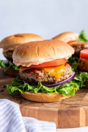 Turkey burgers with cheese, tomato, and lettuce on a wood platter.