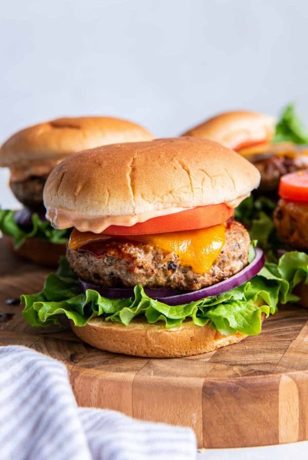 Turkey burgers with cheese, tomato, and lettuce on a wood platter.
