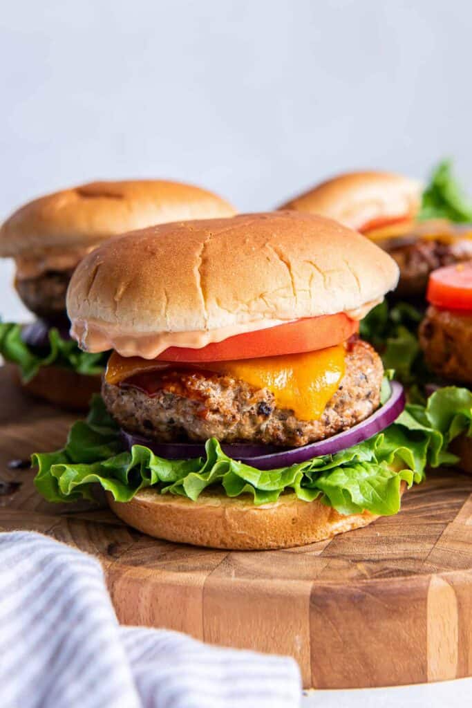 Turkey burgers with cheese, tomato, and lettuce on a wood platter.