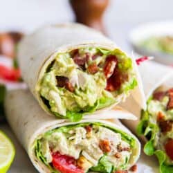 A chicken avocado salad wrap sliced in half and stacked on parchment paper.