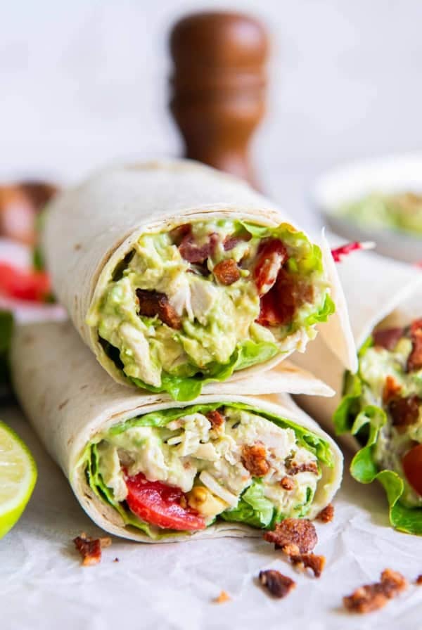 A chicken avocado salad wrap sliced in half and stacked on parchment paper.