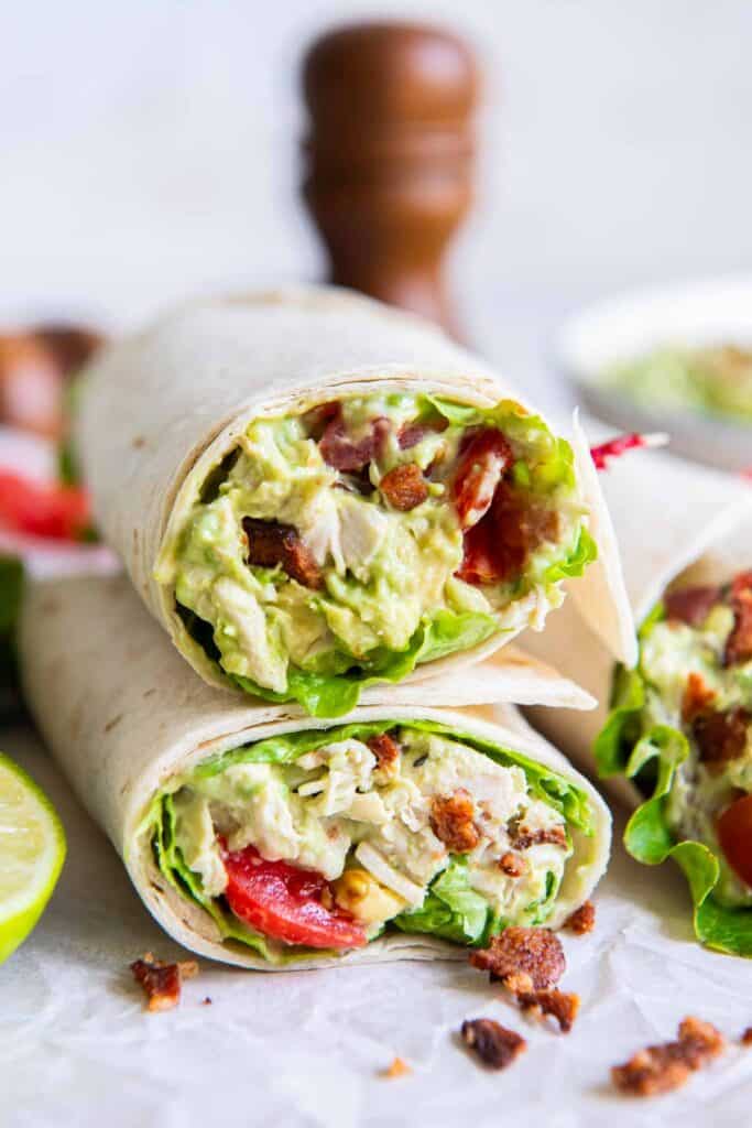 A chicken avocado salad wrap sliced in half and stacked on parchment paper.