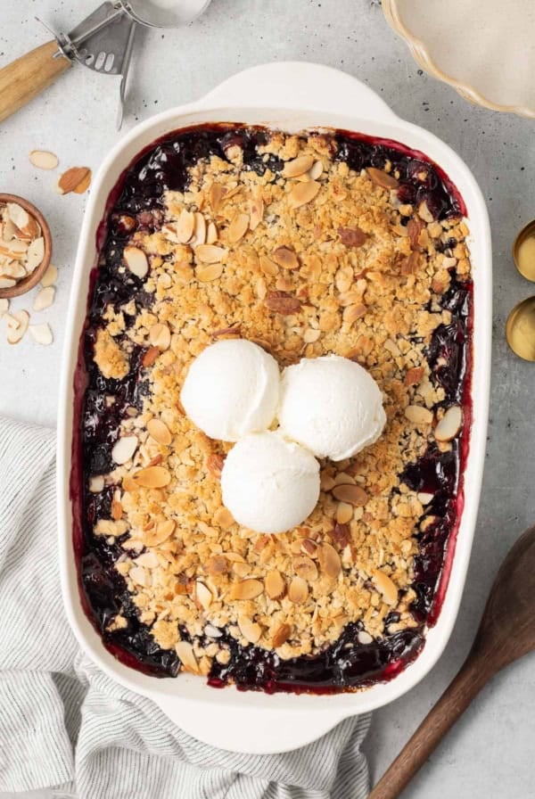 Three scoops of ice cream on top of cherry crisp in a white baking pan.